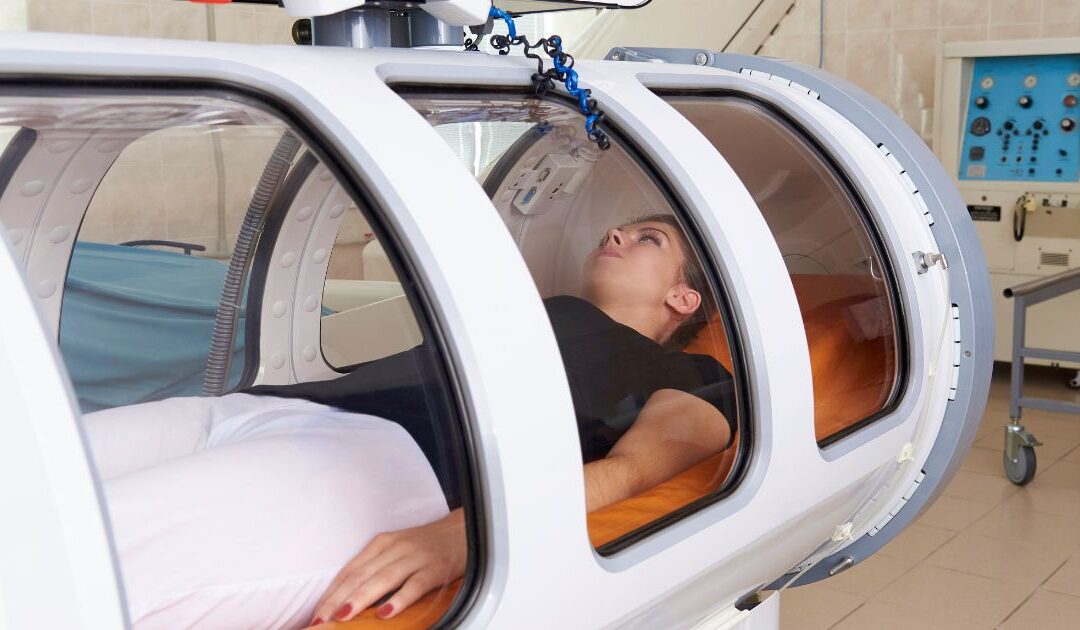 A person is lying comfortably inside an oxygen-rich hyperbaric chamber in a modern medical facility.